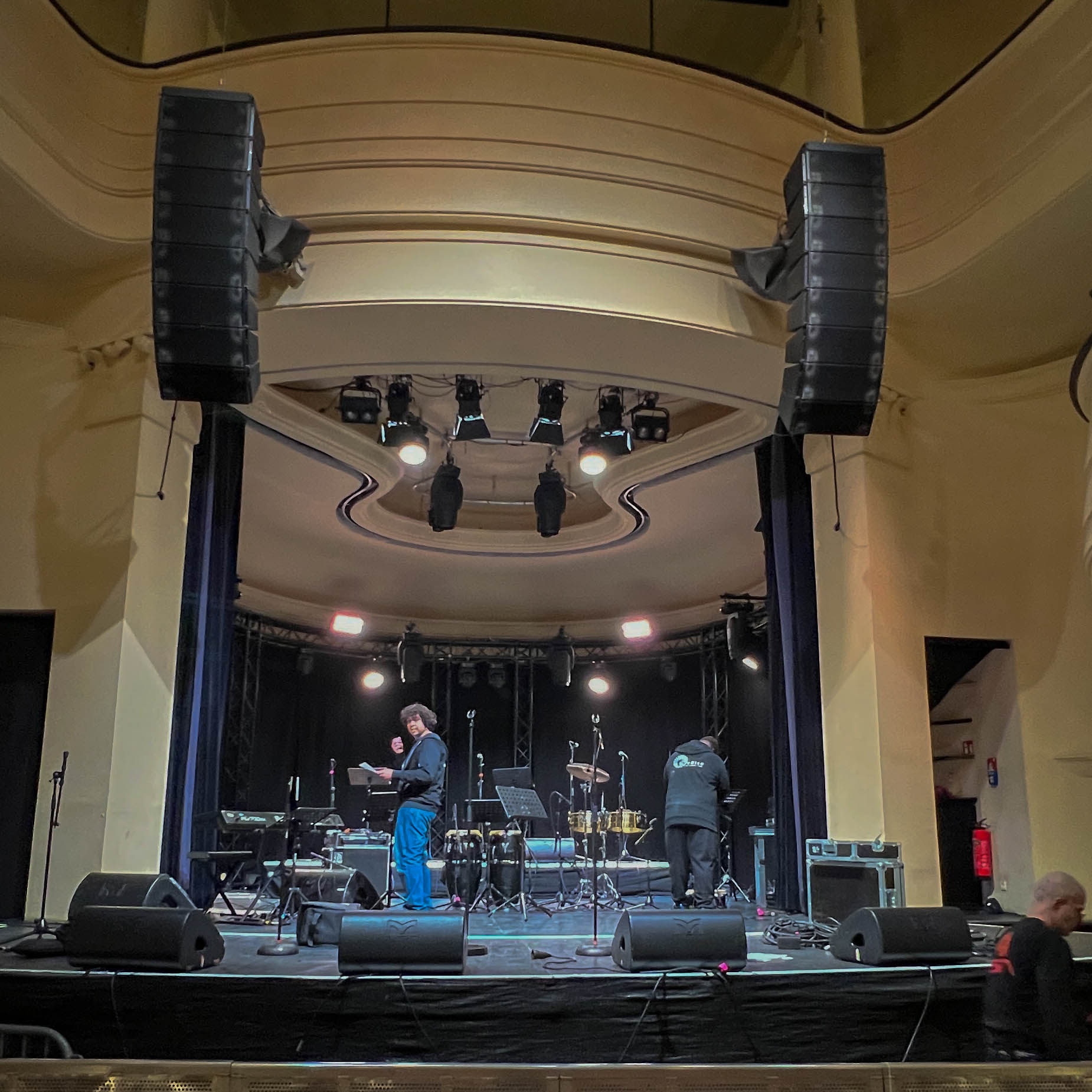 Techniciens dos tournés réglant un système de sonorisation dans une salle d'événement, noir et blanc avec un accent orange
